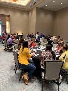 A large meeting room filled with people sitting at round tables.