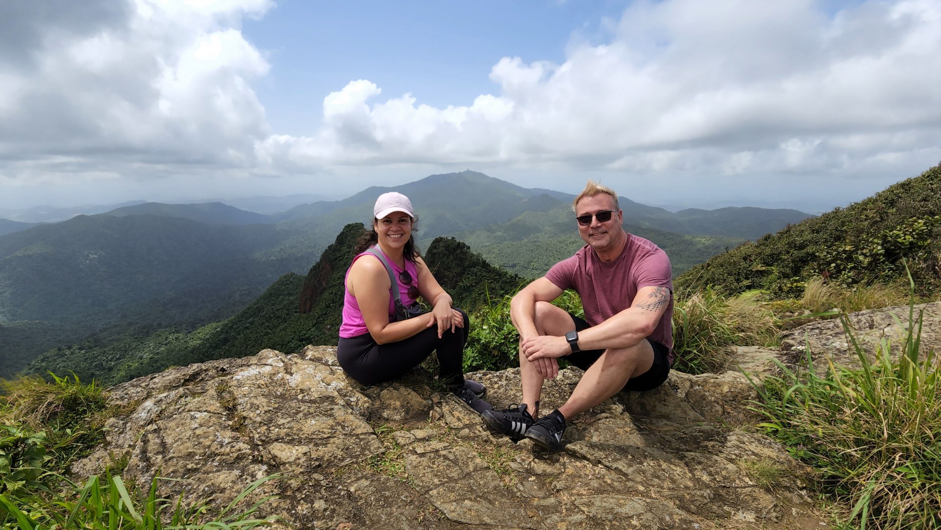 Taina & Jeff sitting on a rock at the top of El Yunque with mountains in the background