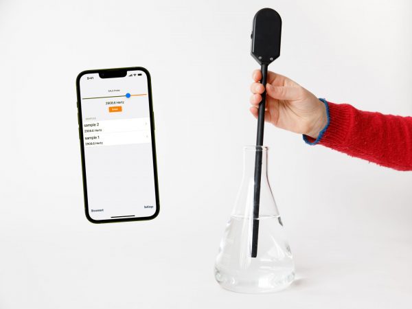 The SALS probe is held in a student's hand with the light detecting tip immersed in a flask filled with colored liquid. A cell phone image is on the right and shows the home screen of the SALS app with two saved sample tones.