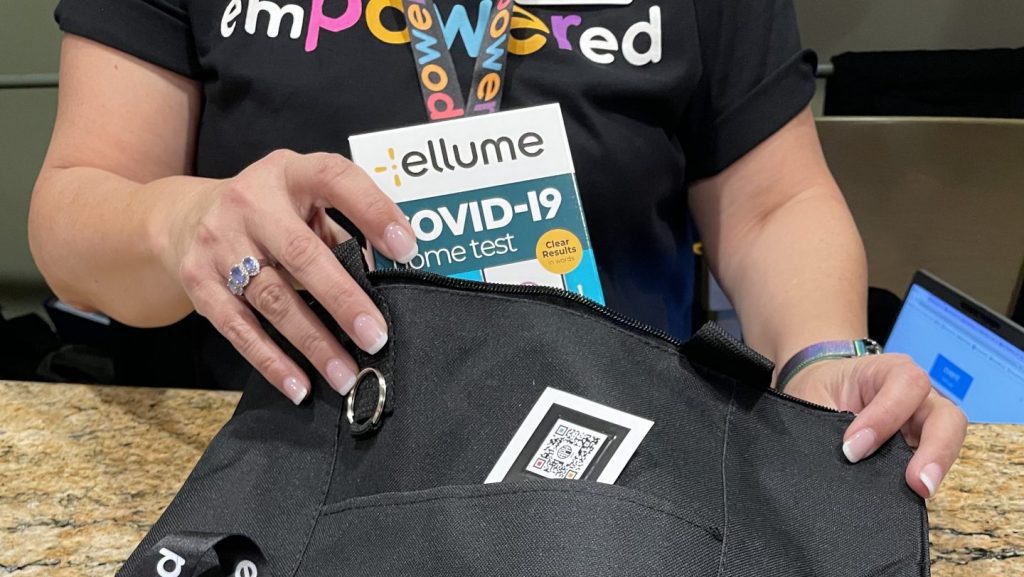 Person wearing an emPOWERed shirt pulling an Ellume accessible COVID-19 test from an bag.