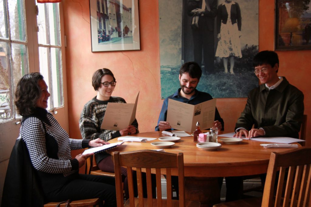 Four people seated at a restaurant and smiling. Two are reading print menus and two are reading braille menus.