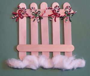 Small fence constructed from popsicle sticks with cotton balls at the bottom and tiny candy canes on the top.