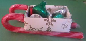 A small paper sleigh full of small candies with runners made out of candy canes.