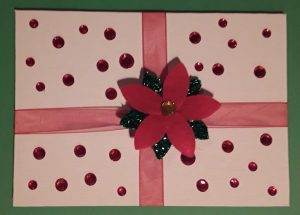 A white card decorated with red ribbon, red sequins, and a felt poinsettia.
