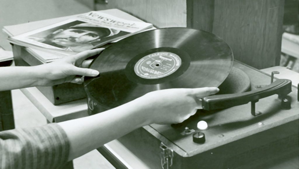 View of a woman’s arms placing a vinyl record on the turntable of the record player.