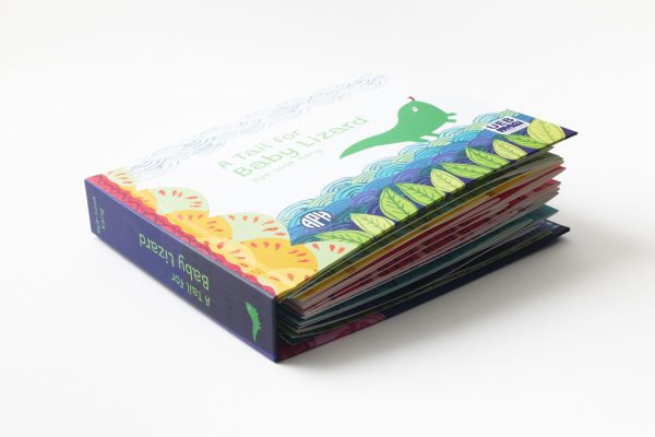 A Tail for Baby Lizard” storybook resting on the back cover. The spine of the book is navy blue and reads, “A Tail for Baby Lizard” in green, with an image of baby lizard at the bottom of the spine also in green.