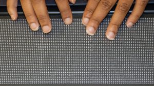 Fingers on a 10 line by 32 cell braille display. The display has raised pins representing a square with plot points on it from a geometry lesson.