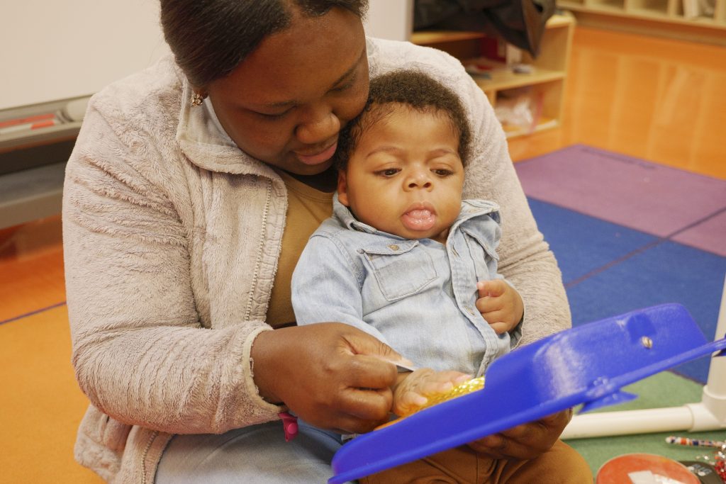 A woman showing the young child sitting on her lap a toy.