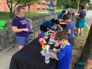 Several APH employees helping children with crafts at a table in front of the APH building.