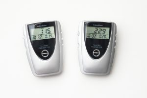 Two, white and black, walking pedometers on a white background. The pedometer on the left shows 115 steps, 0.14 miles walked, and a duration of 10 minutes and 32 seconds. The pedometer on the right, shows 229 steps, 0.28 miles walked, and a duration of 10 minutes and 32 seconds.