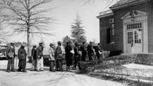 Eleven men, most using canes and carrying braille books, line up, waiting for the library to open.