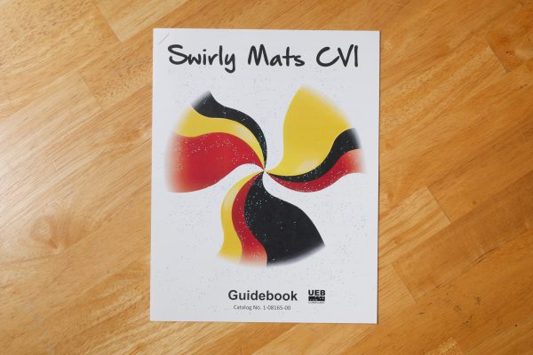 Swirly Mats CVI Guidebook on a wooden surface. Yellow, black, and red swirly mats are shown on the cover of the guidebook.