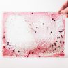 Zoomed out image of a red swirly mat with confetti and glitters over a white background.