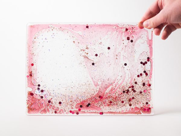 Zoomed out image of a red swirly mat with confetti and glitters over a white background.