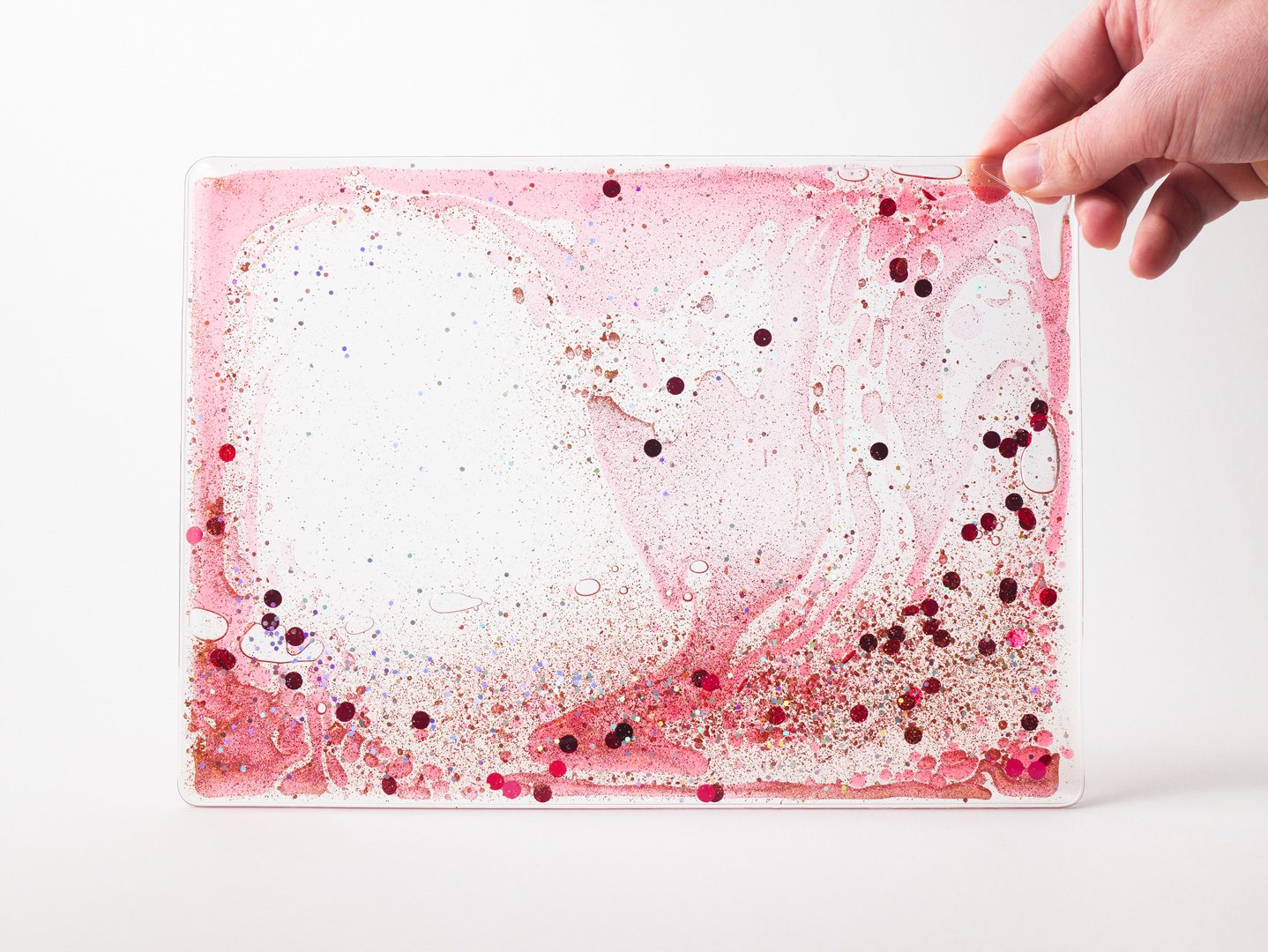 Zoomed out image of a red swirly mat with confetti and glitter over a white background.