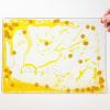 Zoomed out image of a yellow swirly mat with smiley faces and glitters inside the mat, over a white background.