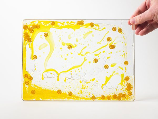 Zoomed out image of a yellow swirly mat with smiley faces and glitters inside the mat, over a white background.