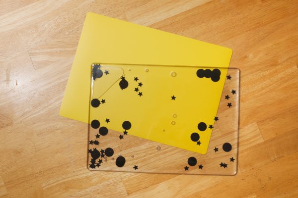 Black swirly mat with stars and circles on the inside placed on top of a yellow tabletop mat.