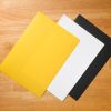 Tabletop mat pack on top of a wooden surface. The color and order of the mats are yellow, white, and black.