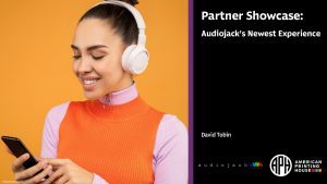 Partner Showcase webinar banner. A woman wearing headphones and using a smartphone. Text reads: "Partner Showcase: Audiojack's Newest Experience. David Tobin." Audiojack logo. APH logo.