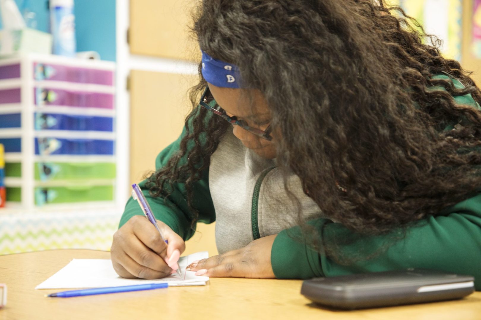 A teenage girl writing on a notebook in a classroom.