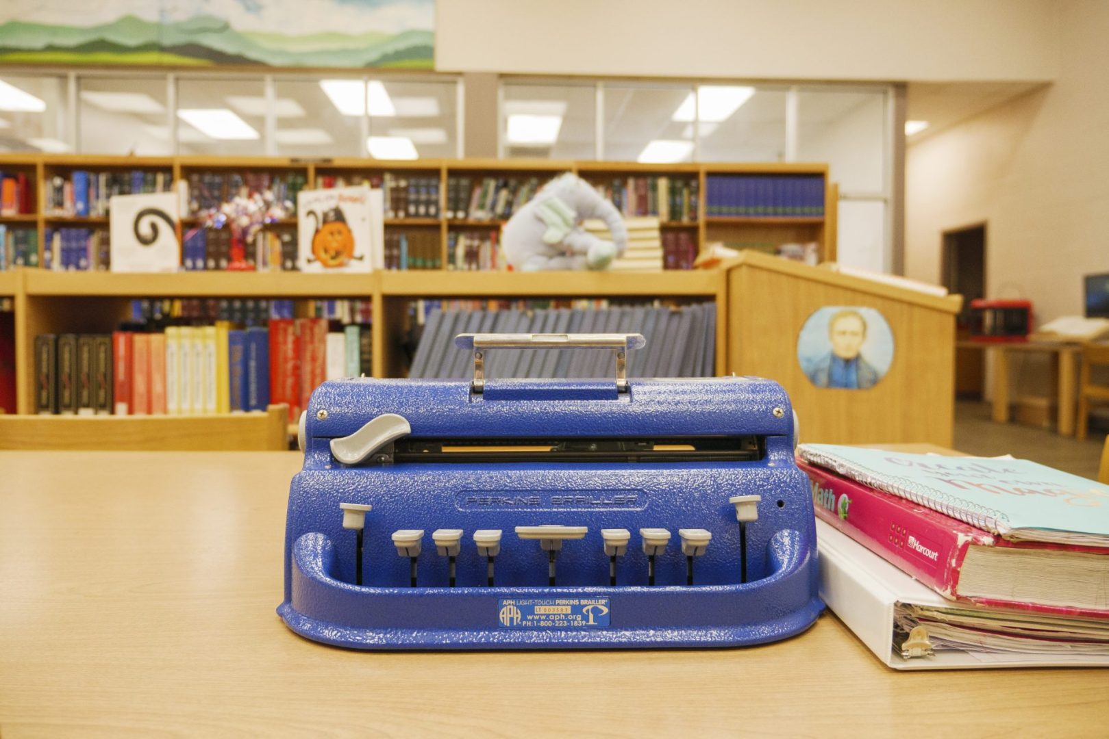 A Light-Touch Perkins Brailler sits on a wooden table in a school library.