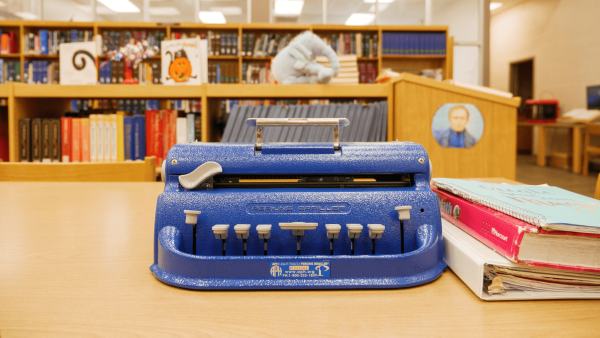 A Light-Touch Perkins Brailler sits on a wooden table in a school library.