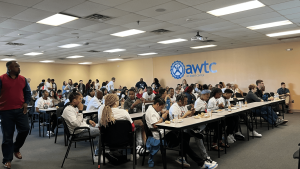 Several rows of students in white tshirts sitting at long tables.