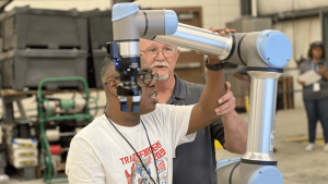 An instructor shows a student how to use a large robot arm.