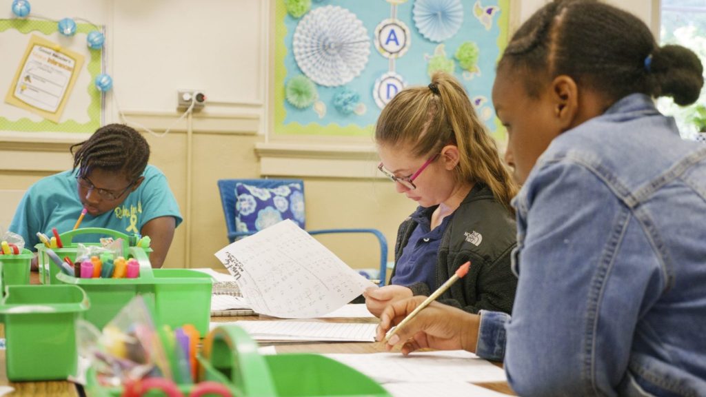 Three students sit at a table and work on math problems in a classroom.