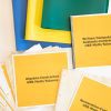 Close-up of KeyMath 3 UEB Supplement Contracted kit displaying three folders (blue, yellow, and green) and three instruction booklets: Written Computation Subtests, Algebra, and Numeration-Contracted UEB Math/ Science.