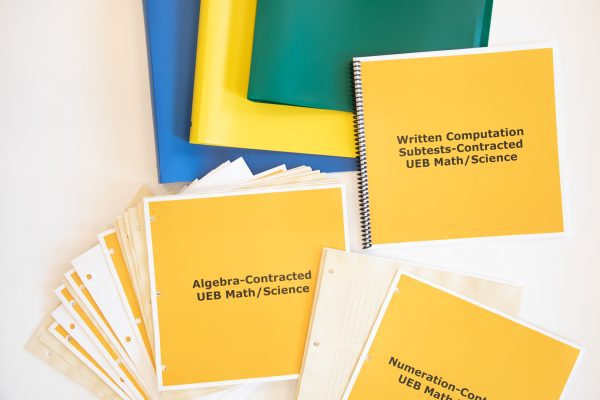 Close-up of KeyMath 3 UEB Supplement Contracted kit displaying three folders (blue, yellow, and green) and three instruction booklets: Written Computation Subtests, Algebra, and Numeration-Contracted UEB Math/ Science.