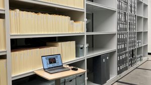 Rows of shelves in the Museum Archives, some still filled with boxes, some completely empty.