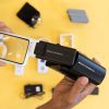Two hands focused in on holding a white rectangular magnifier that is being slid into a black magnifier holder. There are additional optical aids resting over a yellow background.