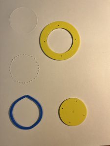 Two GDS manipulatives, and three circular shapes drawn using a stylus and Graph Benders. On the top right is a yellow outer circular stencil. On the top left is a solid-line circle and dotted-line circle drawn by tracing the inside of the stencil with the stylus. On the bottom right is a yellow inner circular stencil, and the bottom left features a circle drawn with Graph Benders.