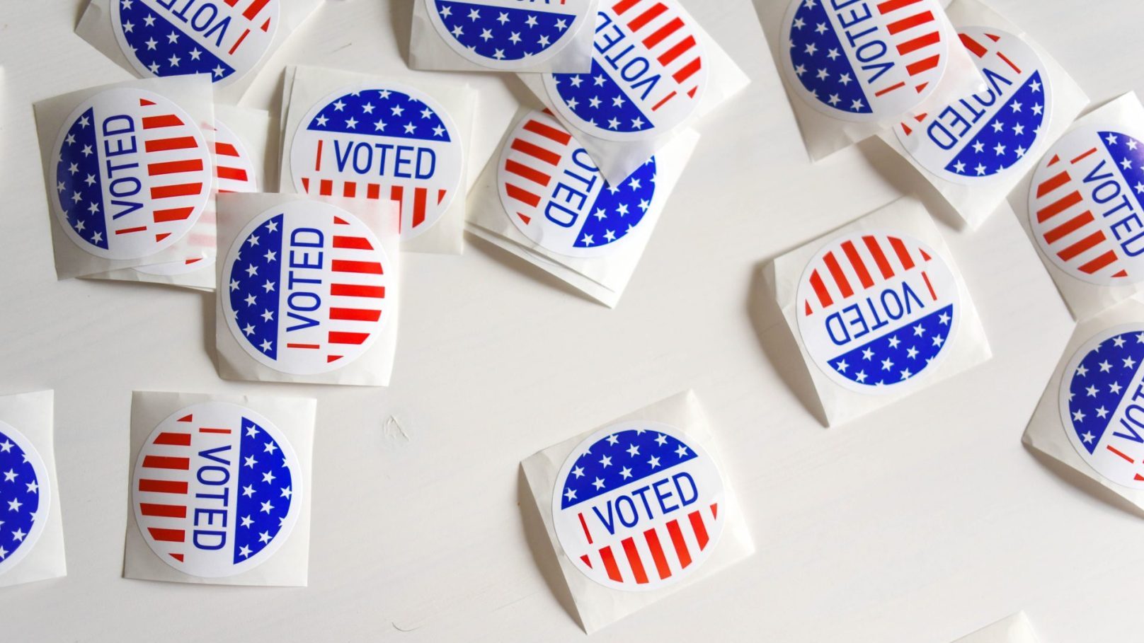 Round stickers reading “I VOTED” with starts and stripes reminiscent of the ones on the American flag scattered across a white background.