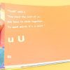 A hand holding an orange open page of Alphabet Scramble that shows large print text in line with braille.