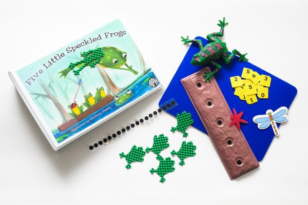 The Five Little Speckled Frogs binder and tactile components laid out on a white background. The kit includes a storyboard, tactile frogs and dragonflies, a log, and combination large print and braille number cards. On the cover of the binder is an illustration of one speckled frog leaping off the hollow log into a pond of blue water. Three frogs remain on the log, and one is catching a dragonfly with its tongue.