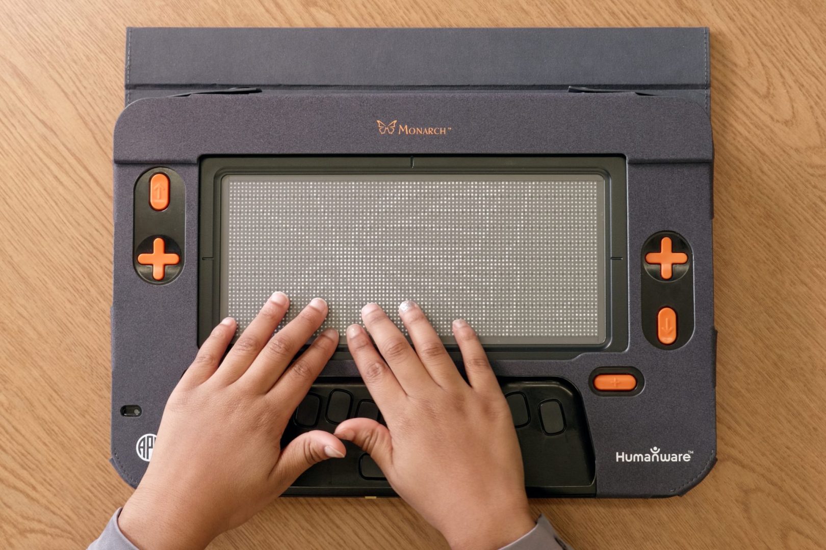 A child's hands feels The Monarch’s 10 line by 32 cell refreshable braille display, which is displaying a tactile graphic of a monarch butterfly.