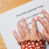 A close-up of two hands reading the braille on the first page of Five Little Speckled Frogs. Braille is embossed between lines of large print.