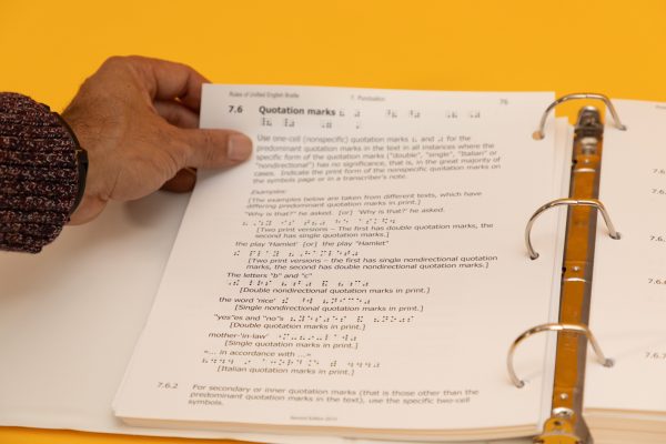A hand holding one corner of a page of an open Rules of UEB large print binder. The information on the page pertains to differences between single and double quotation marks.