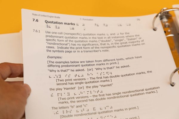 Close up of a hand holding a page in the Rules of UEB large print binder. The information on the page pertains to differences between single and double quotation marks.