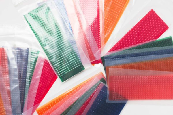 An assortment of dotted, dashed, railroad, and greater-than-sign line path strips in their housing bags laid against a white background. There are blue, yellow, red, green, and clear strips of each texture.