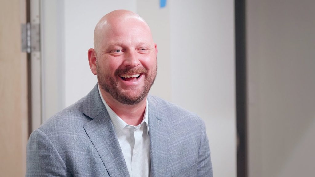 Wayne Price smiles while wearing a gray suit jacket and a light colored shirt.