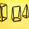 Three-dimensional shapes created using this Geometro pack with the Geometro medium kit. From left to right, there is a rectangular prism, a right triangular prism, and a triangular pyramid, all against a yellow background.