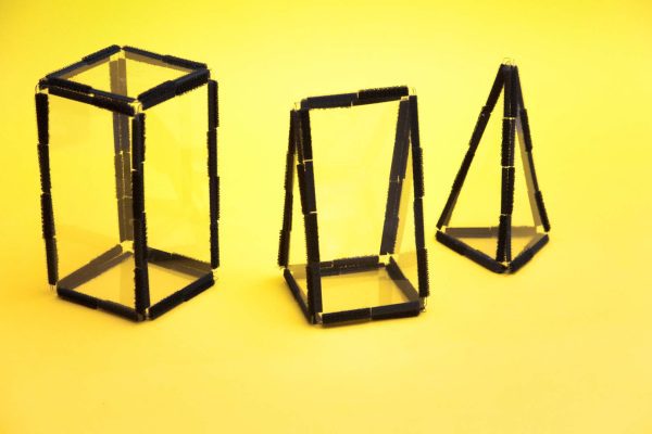 Three-dimensional shapes created using this Geometro pack with the Geometro medium kit. From left to right, there is a rectangular prism, a right triangular prism, and a triangular pyramid, all against a yellow background.