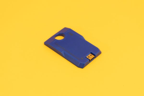 Overhead view of the blue digital talking book cartridge on a yellow background. The cartridge has a circular hole on one end and a USB port on the other, and it reads "4GB."