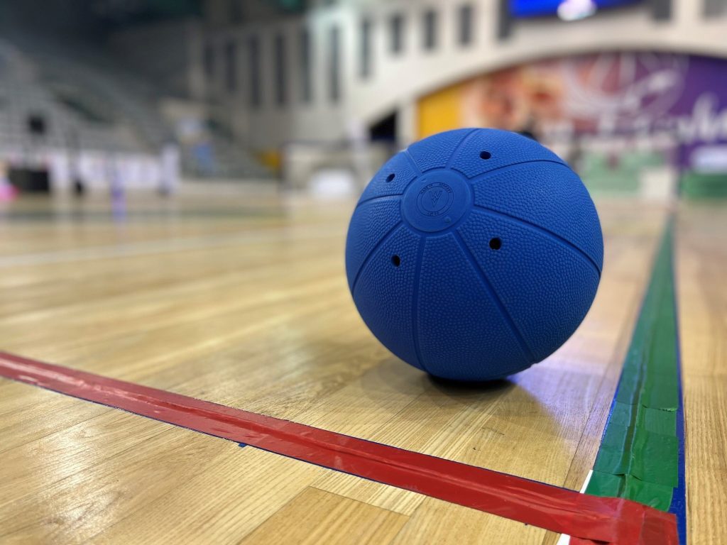 A blue goalball resting on a goalball court.