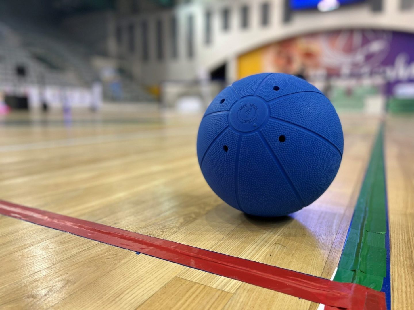 A blue goalball resting on a goalball court.