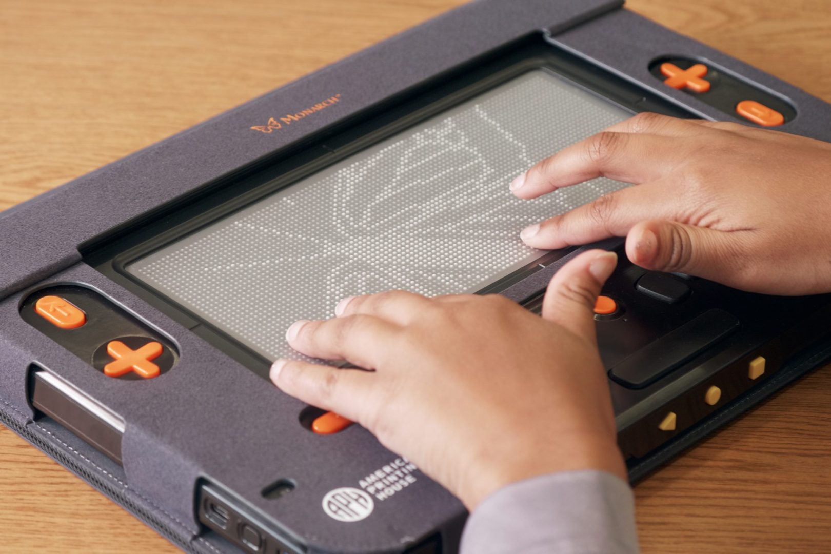 A woman's hands touch a tactile graphic of a monarch butterfly displayed on the Monarch's 0 line by 32 cell refreshable braille display.